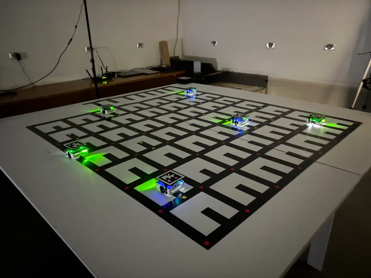 Six illuminated Alvik rovers with AprilTags on their top plates navigating a large printed grid on a table in a darkened lab