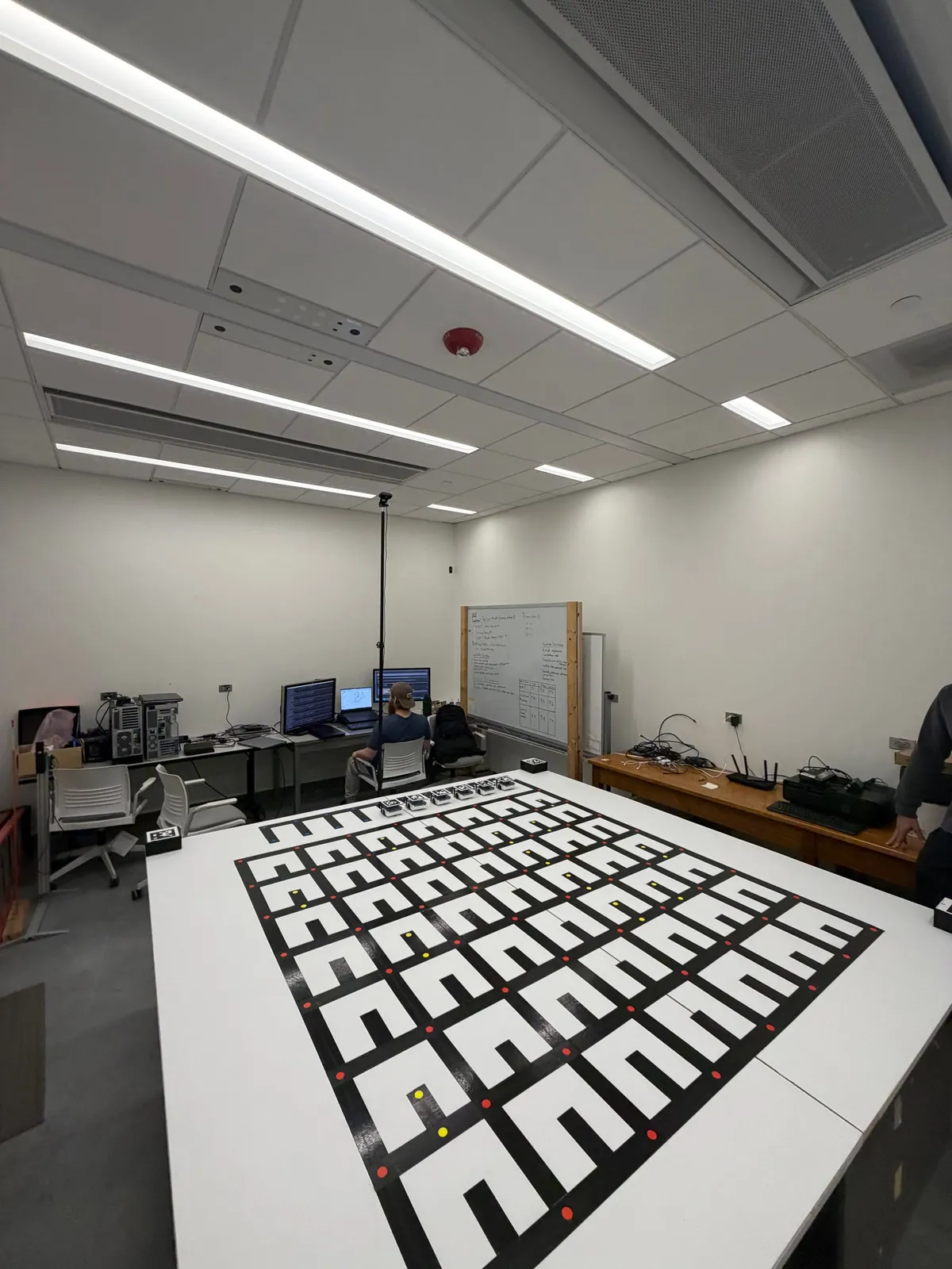 Lab support room with a large printed grid table for robot testing, workstations, and a whiteboard