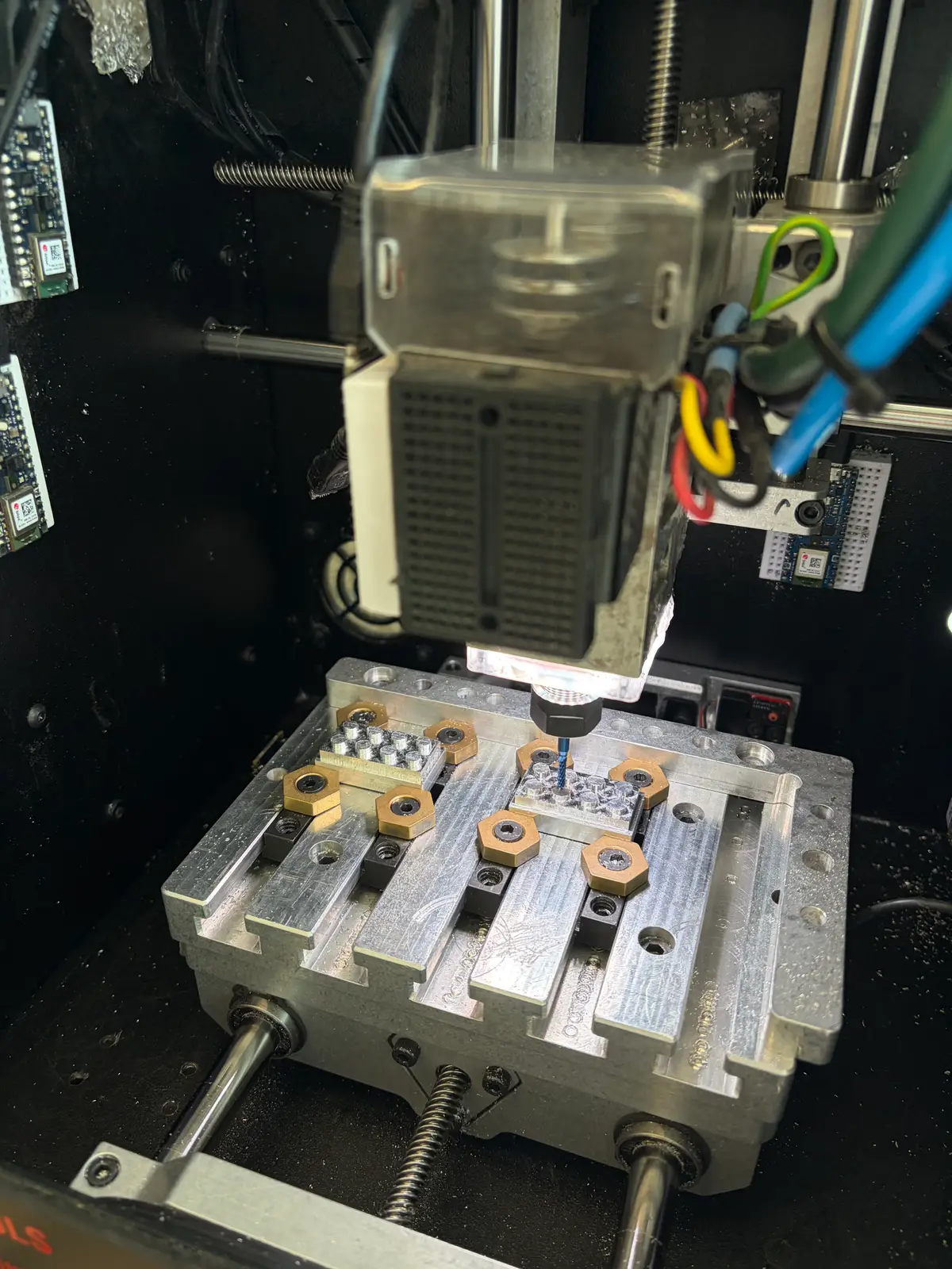 Milling spindle above an aluminum fixture plate holding small metal brick parts with machined studs