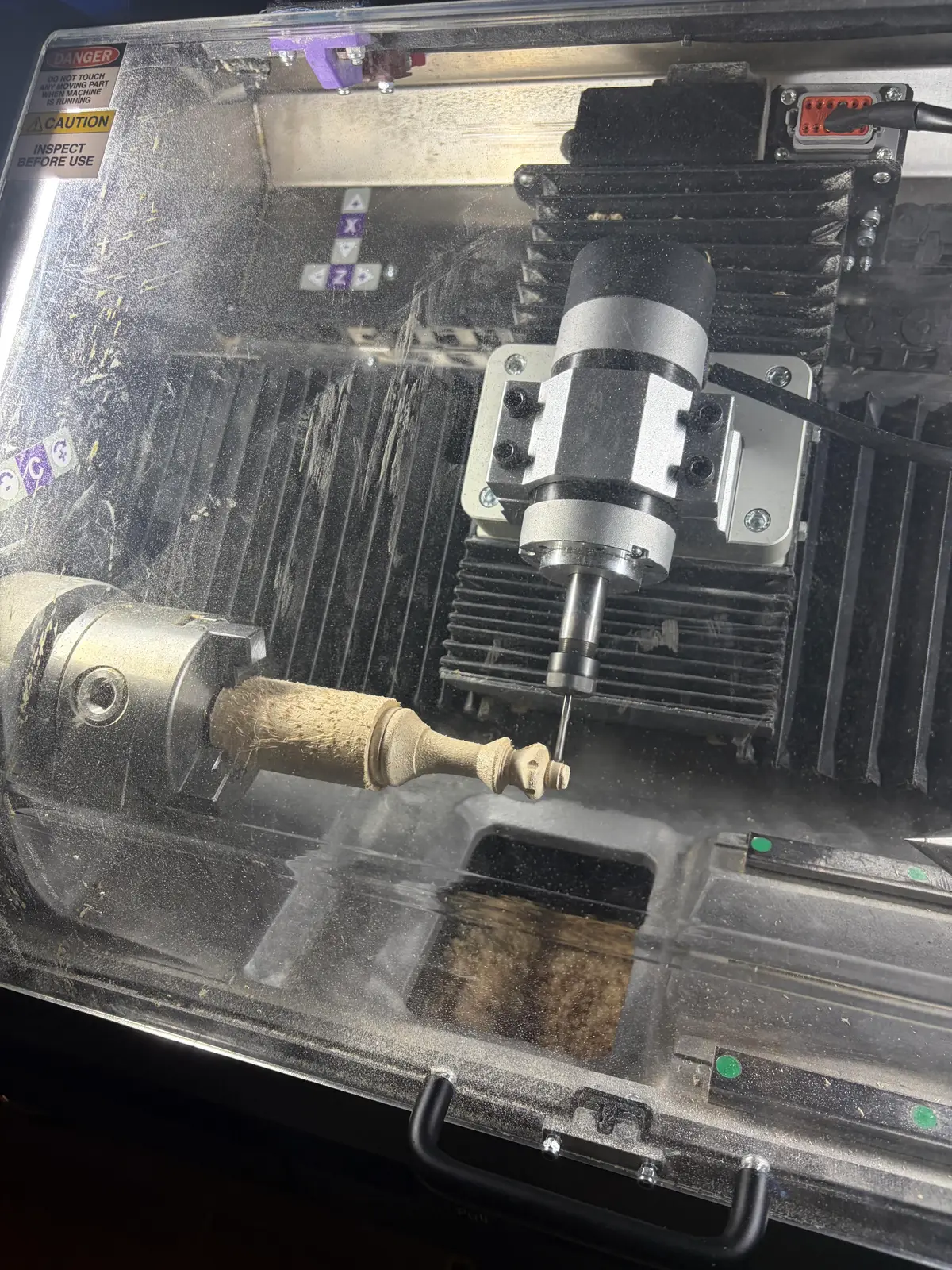 Inside the Rownd enclosure, a turned wooden chess piece held in the rotary chuck beneath the milling spindle