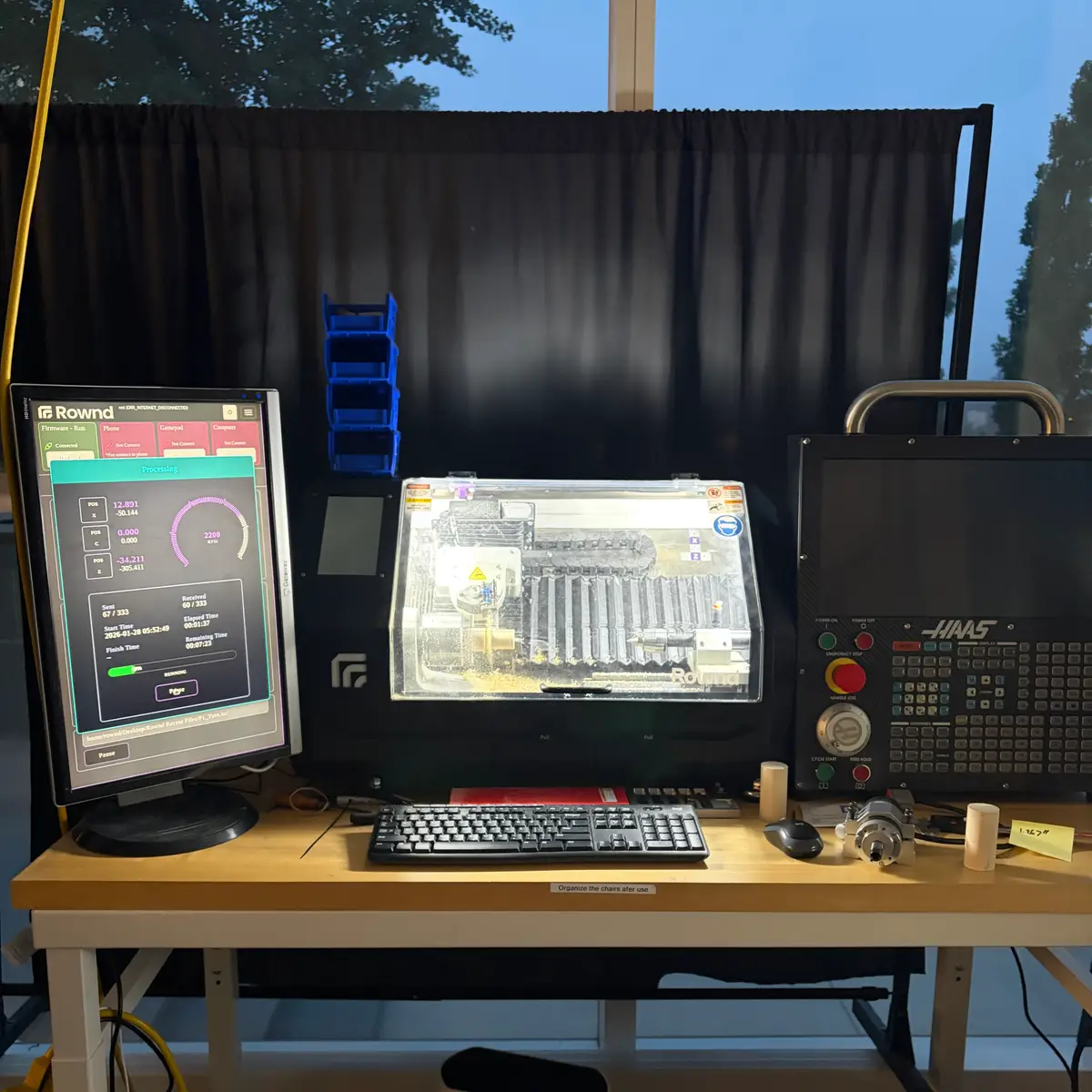 Rownd CNC lathe workstation with its software dashboard on a monitor, the enclosed machine, and a Haas control pendant